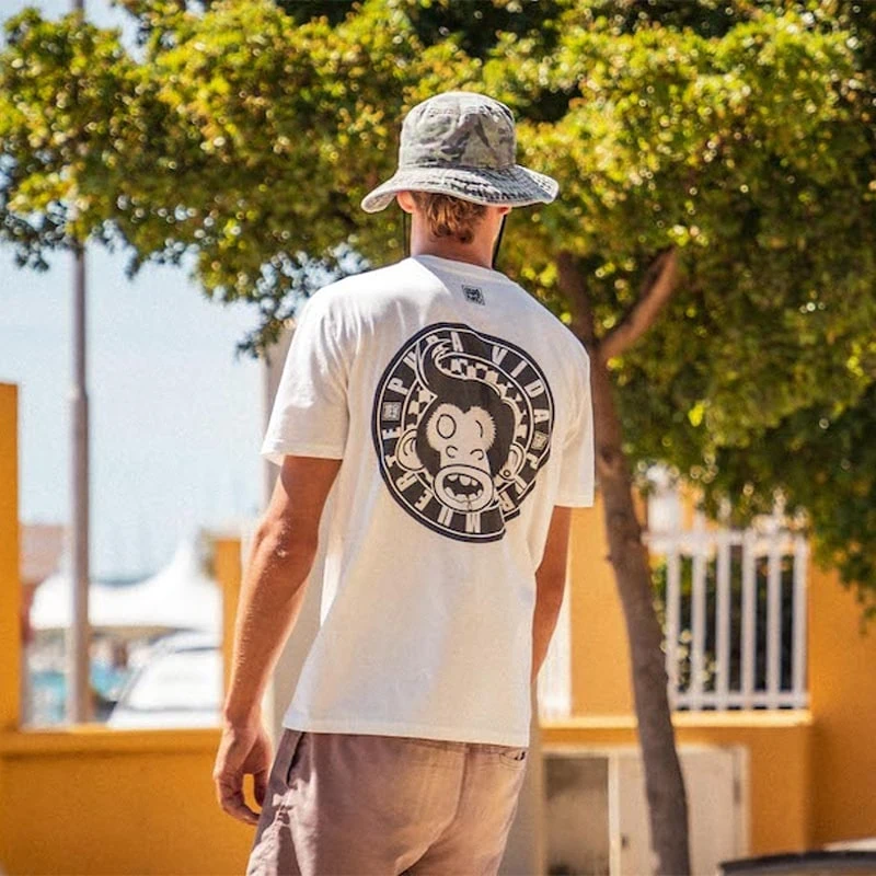 Model walks on Wilhelminaplein in Bonaire wearing a white Swakiko shirt with the design of a monkey's head with a thick quiff and the text 'Pura Vida Pura Muerte'