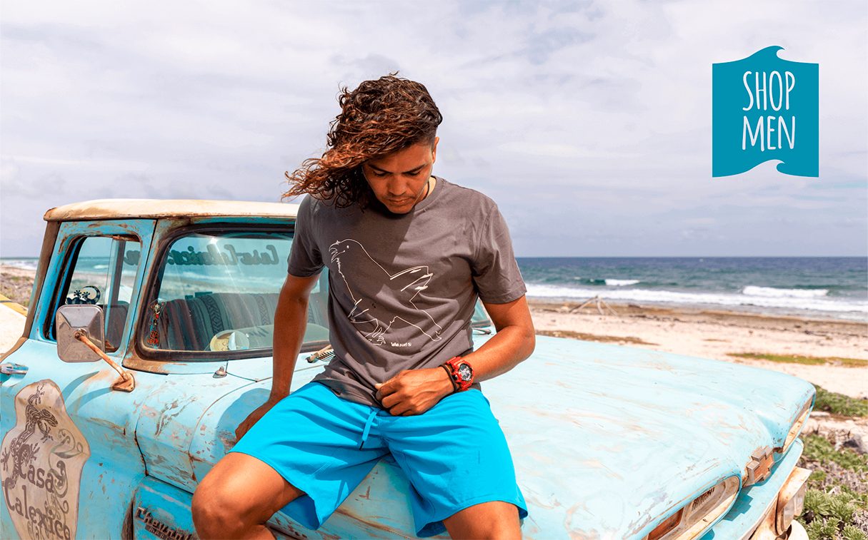 Shop mannen, model zittend op een blauwe Chevy met een artistiek antraciet T-shirt van een kraai met surfboard