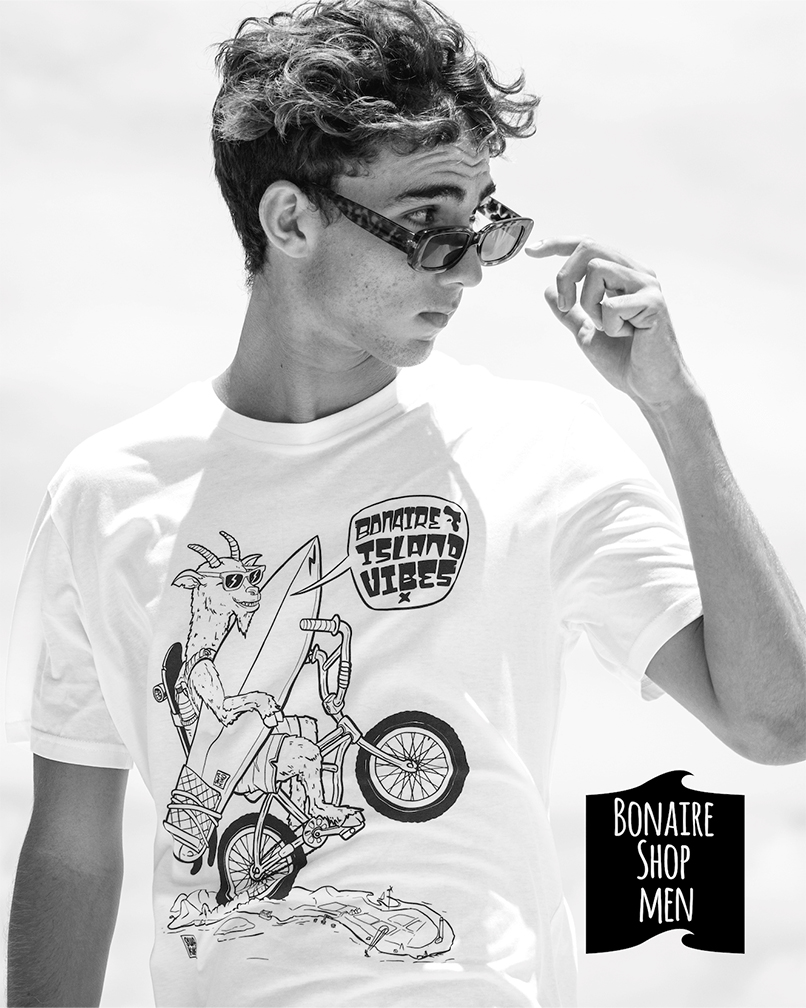 Bonaire Shop mannen: Model met wit T-shirt met geit die op één wiel op een bmx met surfboard in de hand over Bonaire fietst